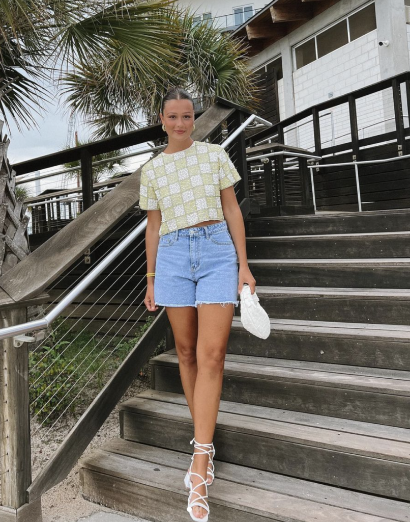A playful pair of denim shorts matched with a crop top creates a relaxed yet fashionable beach ensemble, enhanced with white sandals and a quilted bag.